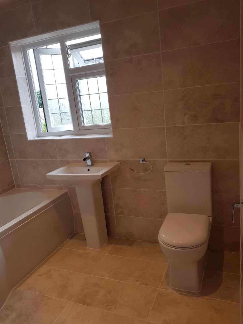 The same bathroom after renovation: stone-effect tiles, new bath, basin and close-coupled toilet