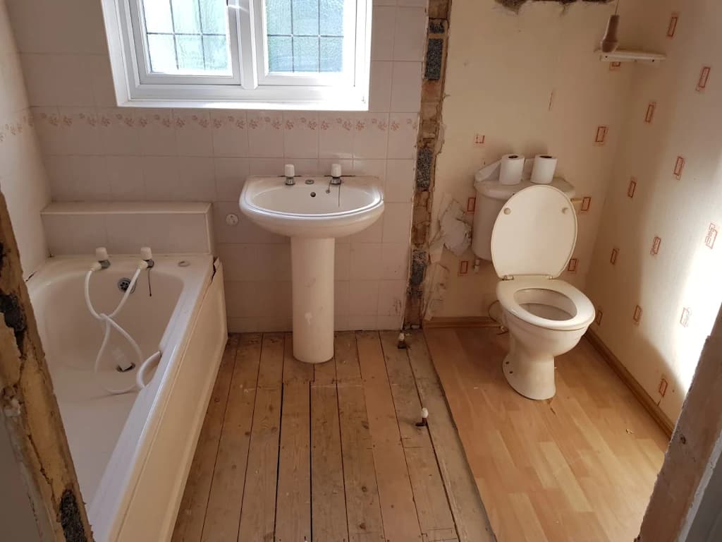 Dated bathroom with worn floorboards and old white suite, before renovation