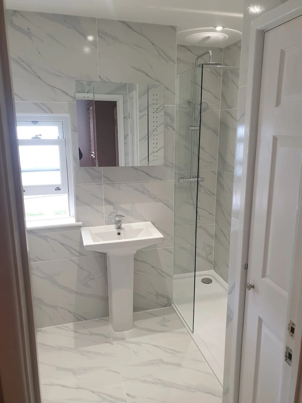 The same room finished as a marble-effect shower room with walk-in shower and pedestal basin