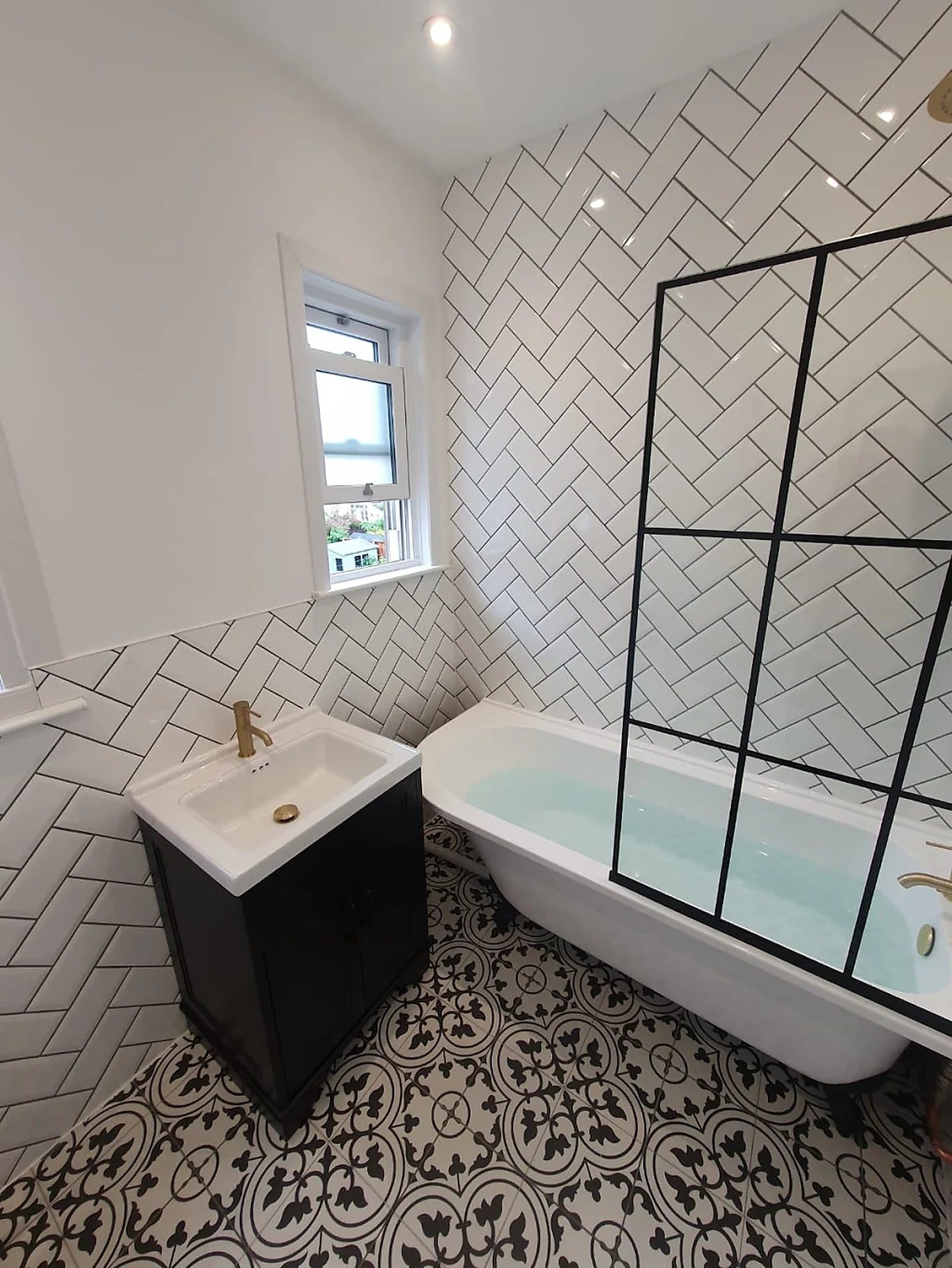 A finished bathroom by DJ's Plumbing Services: bath with a black-framed screen, white metro tiling and a patterned floor